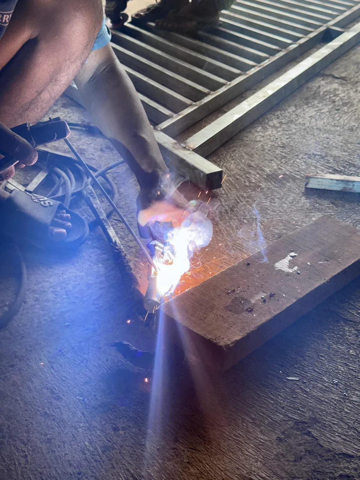 Person welding metal frame, sparks and bright light. Close-up shot with wooden base and metal bars in a workshop.