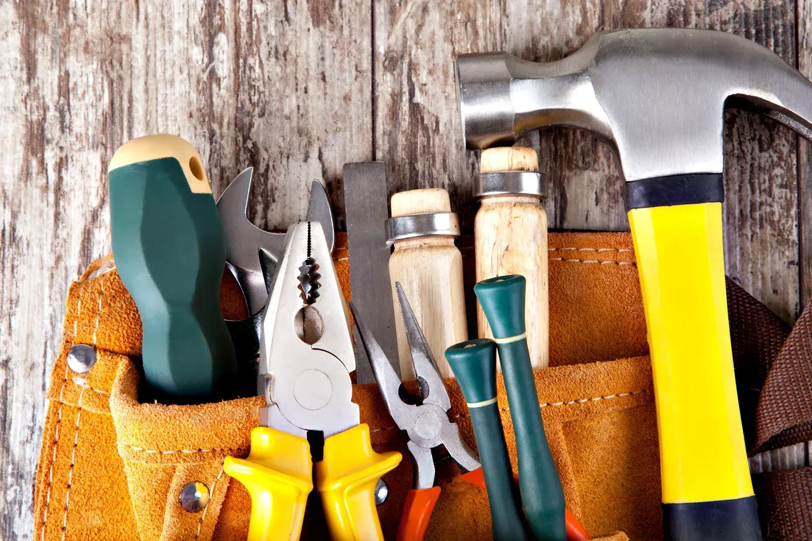 Tool belt with various tools, including a hammer, screwdrivers, and pliers, against a wooden background.