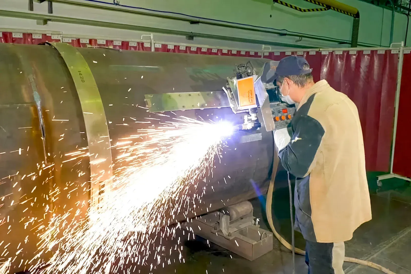 Welder in protective gear cutting metal cylinder, sparks flying.