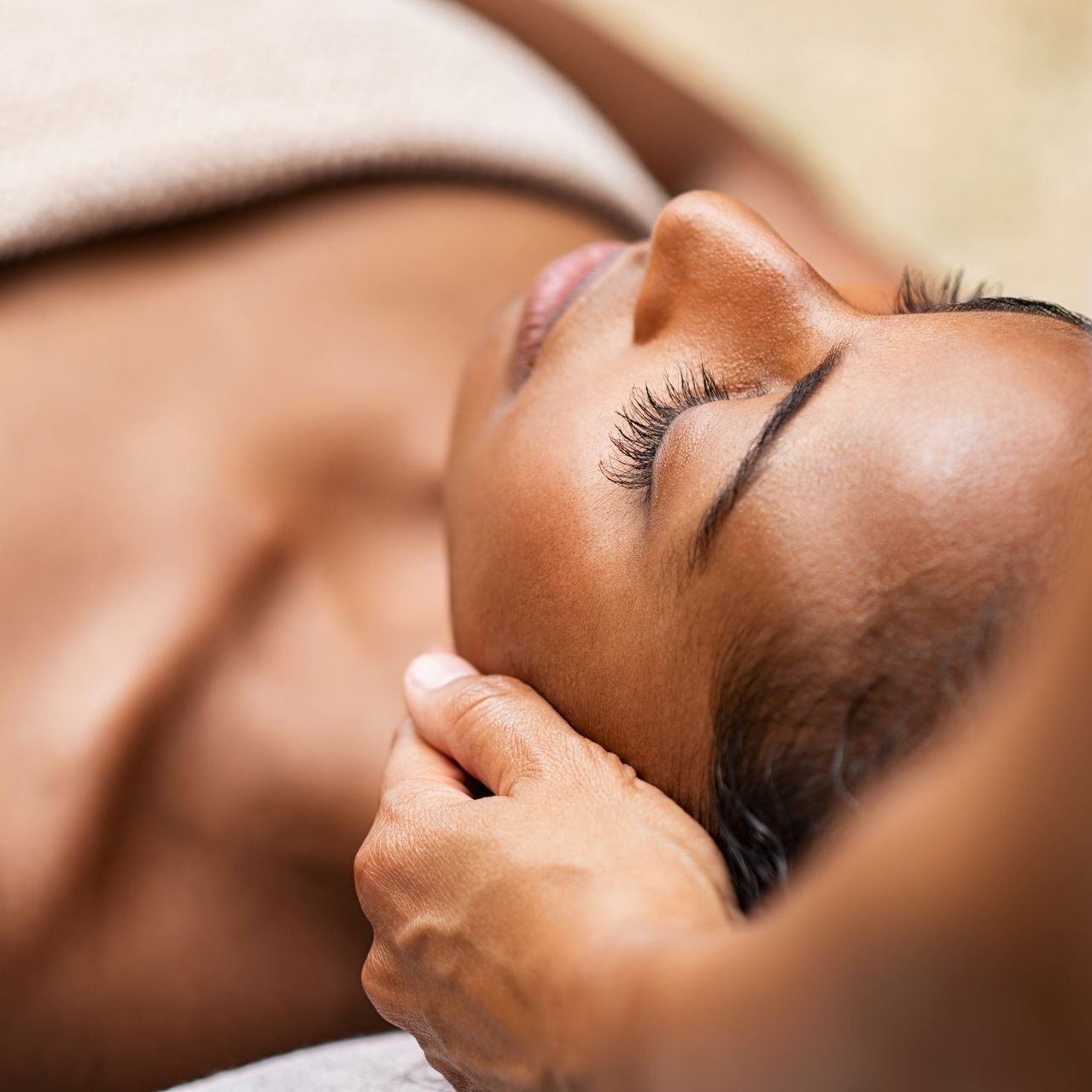 Une femme recevant un massage du cou et de la tête ; détendue, les yeux fermés.