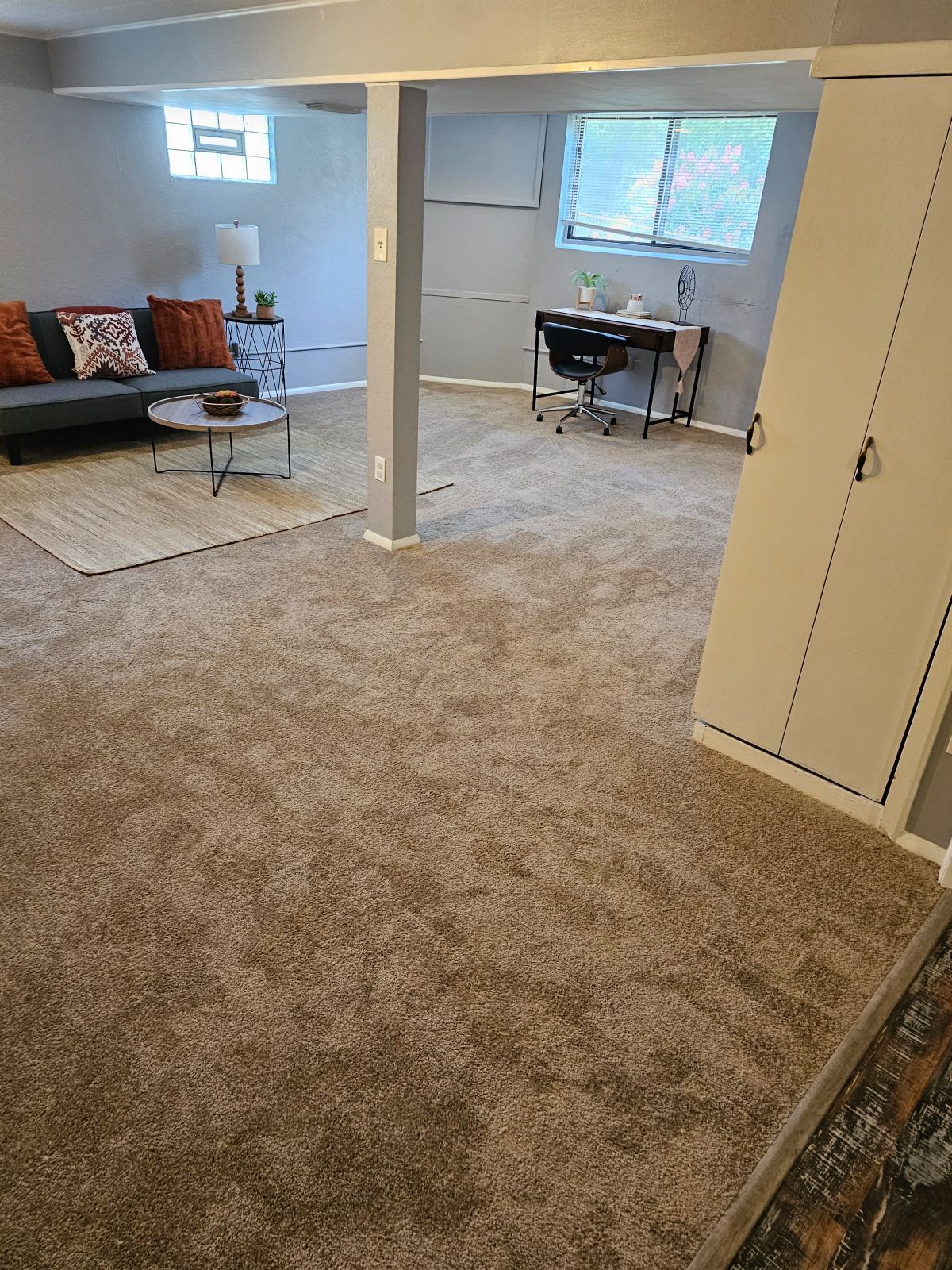 A living room with a couch and a desk in a basement.