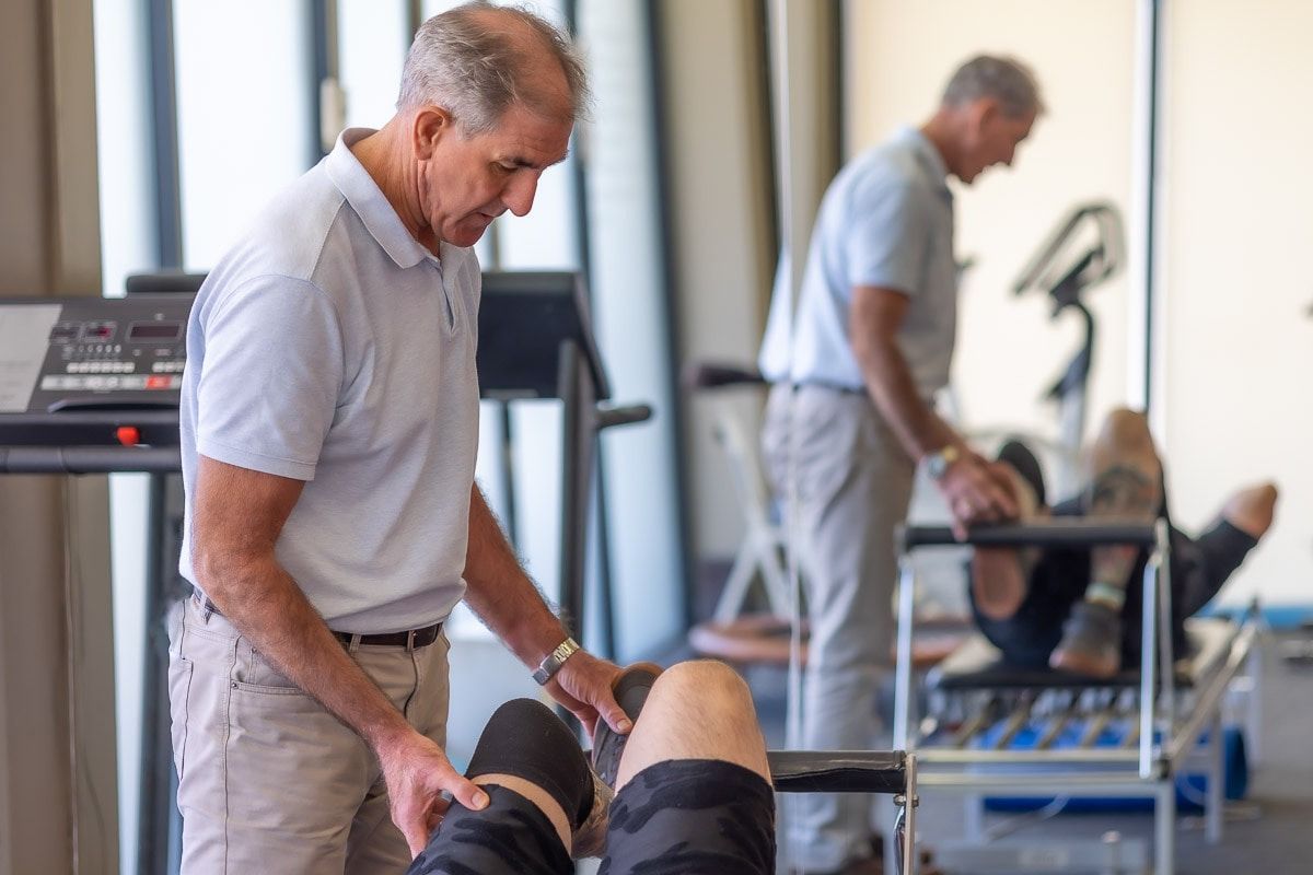 A Man Is Examining A Patient 's Knee In A Gym — Physiocare In Maroochydore, QLD