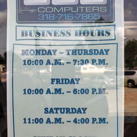 A sign on a window shows the business hours of a computer store.