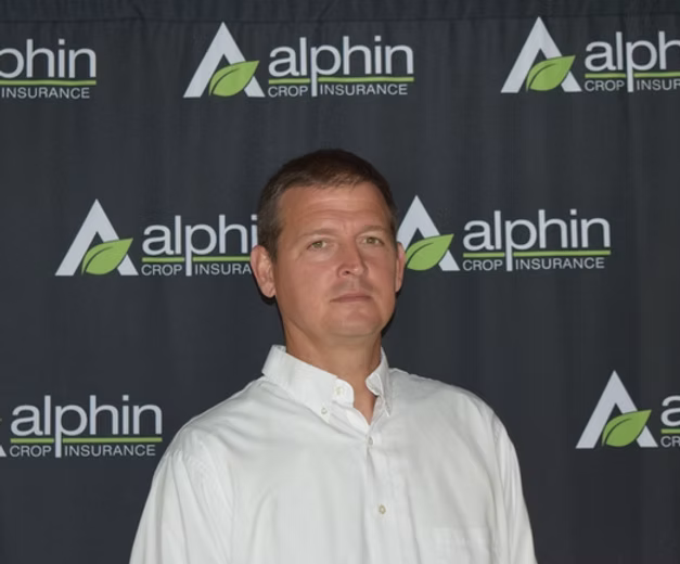 A man in a white shirt stands in front of a backdrop with the 