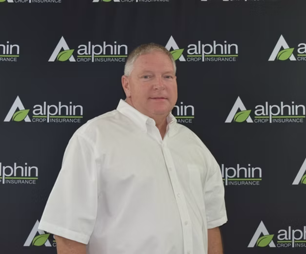 A middle-aged man in a white shirt stands in front of a backdrop with the 