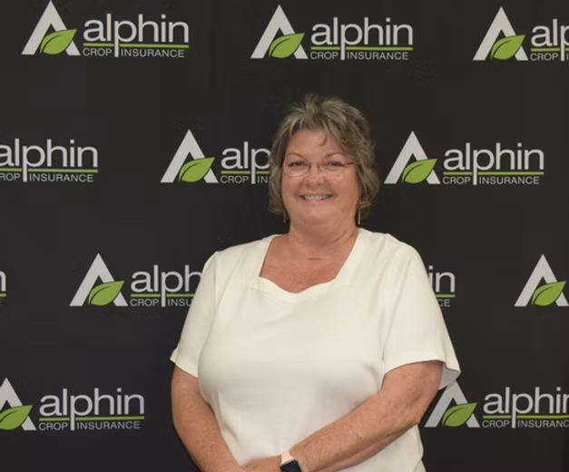 A smiling woman with short brown hair in a white shirt stands in front of a backdrop with 