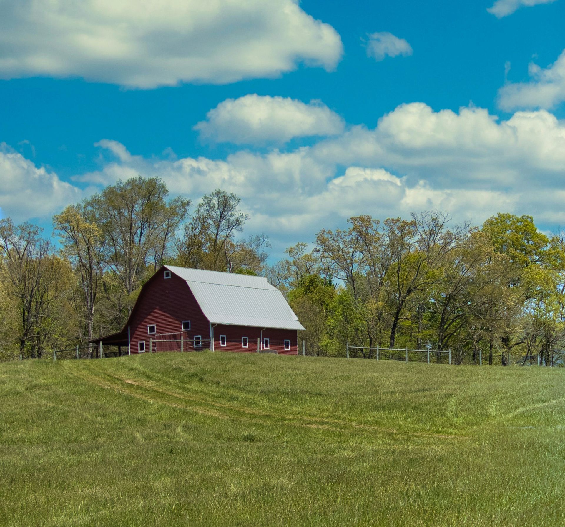 Red barn with a white roof set in a green field under a bright blue sky with fluffy white clouds.