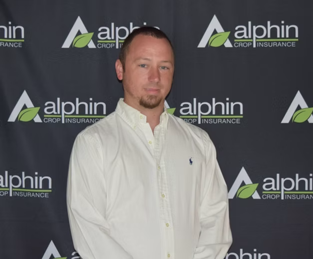 A man with short brown hair and a goatee stands in front of a banner that reads 