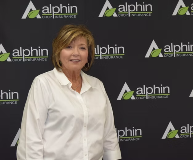 Woman with short blonde hair in a white shirt stands in front of a black backdrop with the 