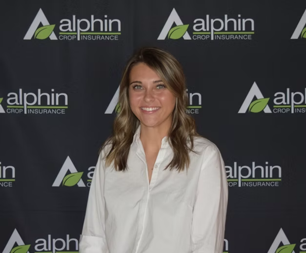 Woman in a white shirt smiling in front of a backdrop with the 