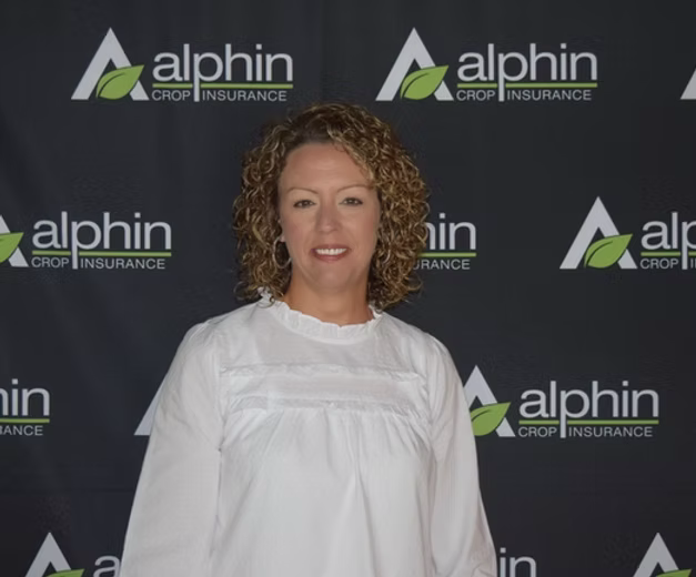 Woman with curly hair in a white blouse poses in front of a backdrop with 