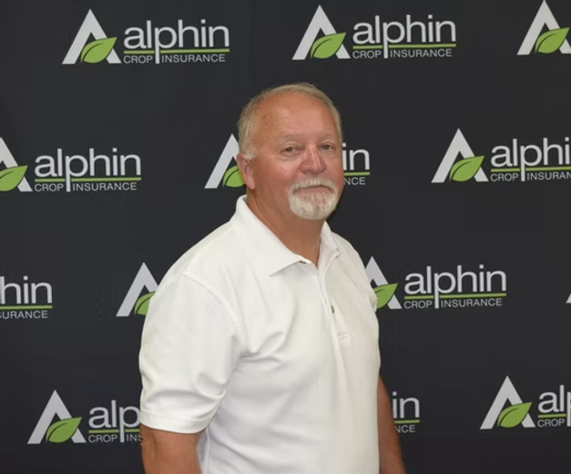 Man with white polo shirt stands in front of a black backdrop with repeating 