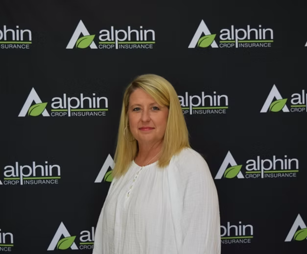 Woman with blonde hair in a white blouse stands in front of a backdrop with the 