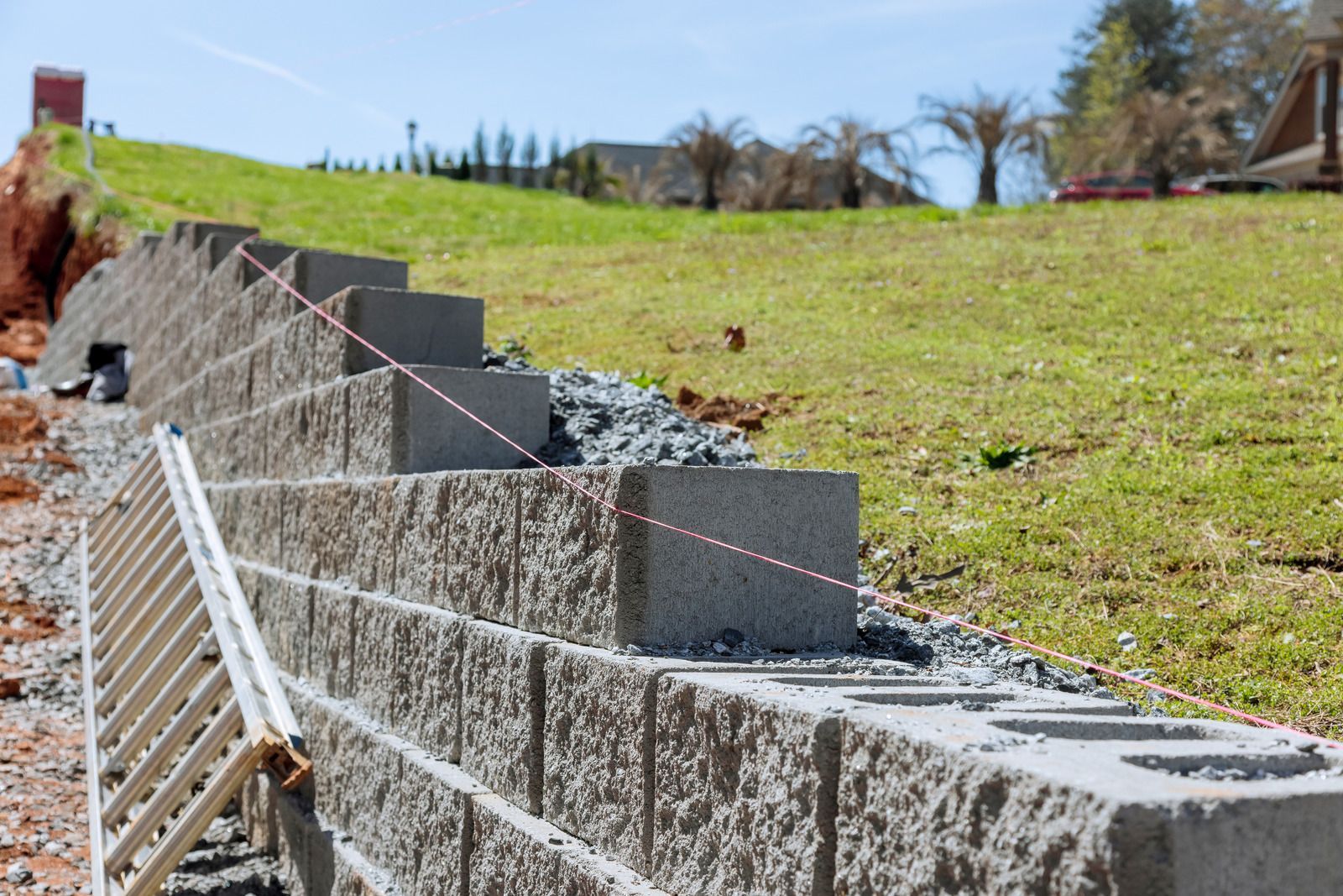 Building a retaining wall with gray concrete blocks on a grassy hillside.