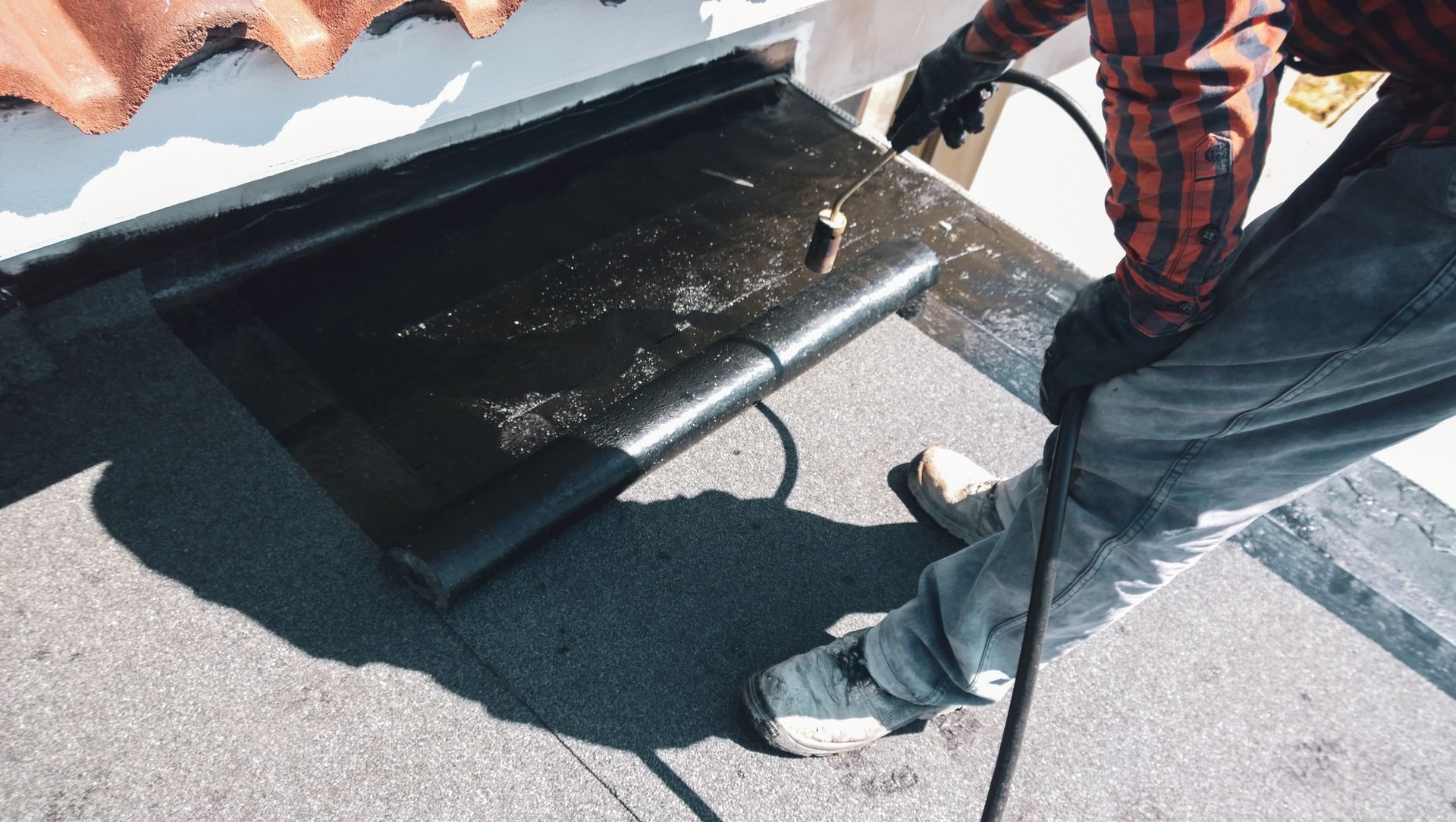 Person using a torch to apply a black roofing material to a flat roof.