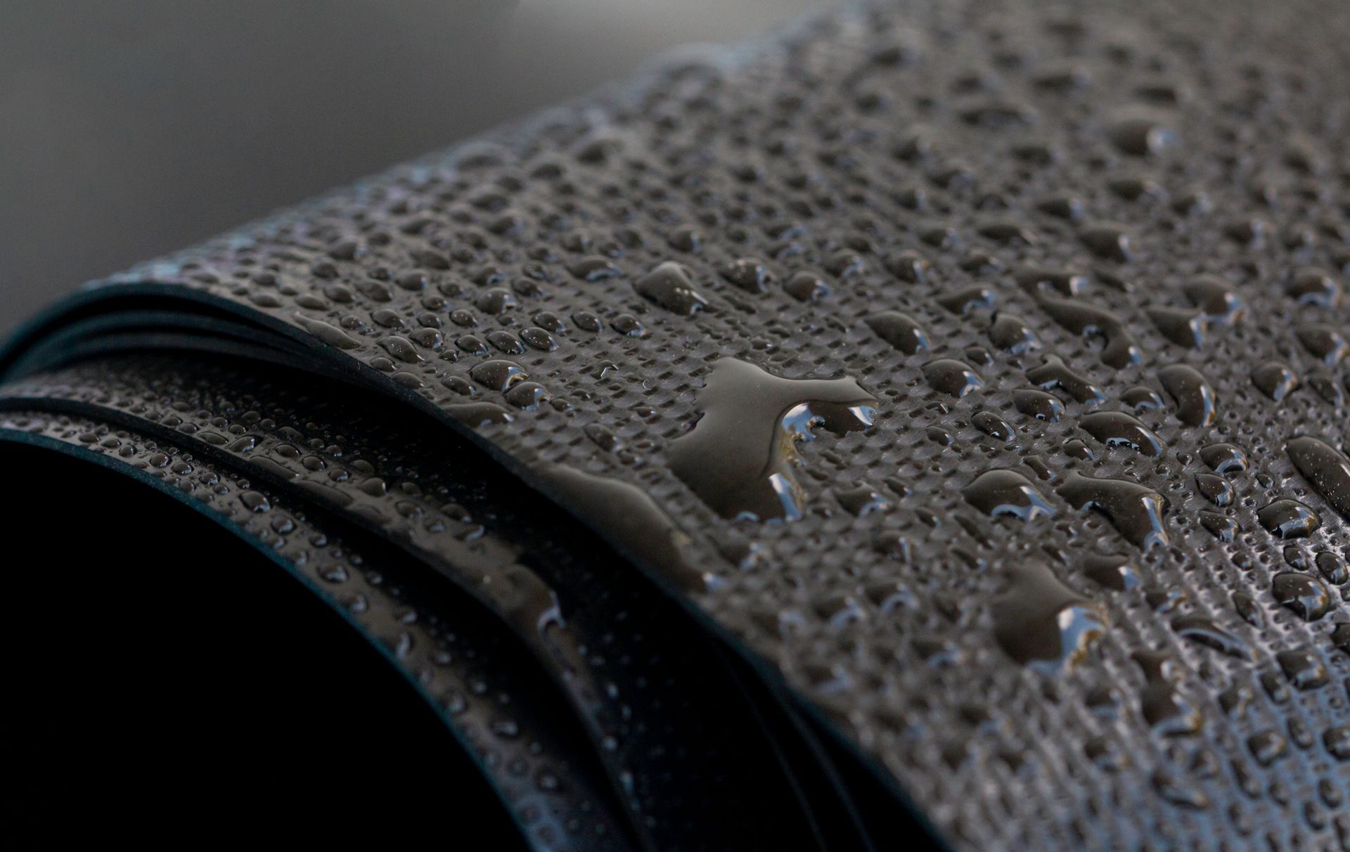 Close-up of a rolled-up, dark gray, textured mat with water droplets on its surface.