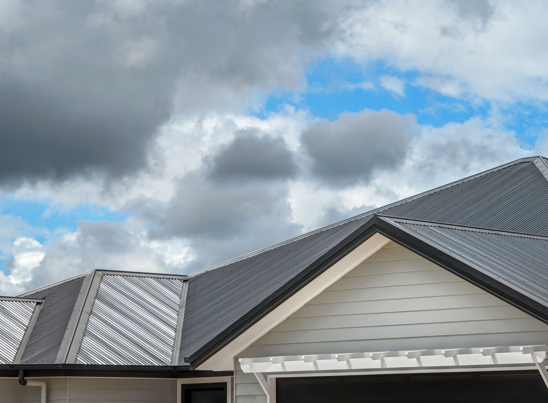 Gray metal roof on a white house against a cloudy blue sky.