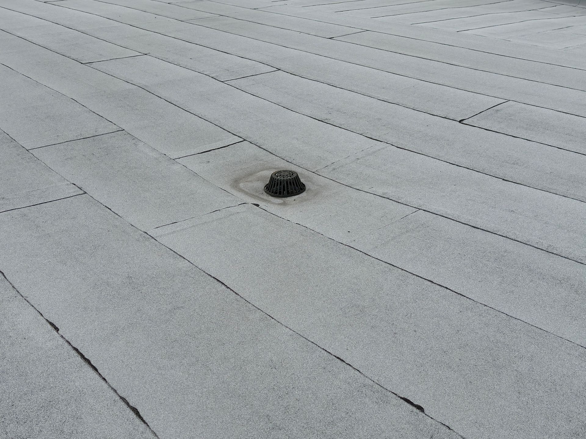 Gray, granular flat roof with visible seams, central drainpipe.