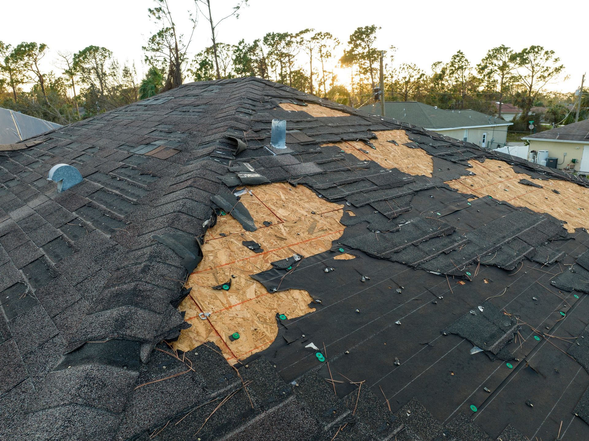 Damaged residential roof with missing shingles and exposed wood, likely caused by a storm.
