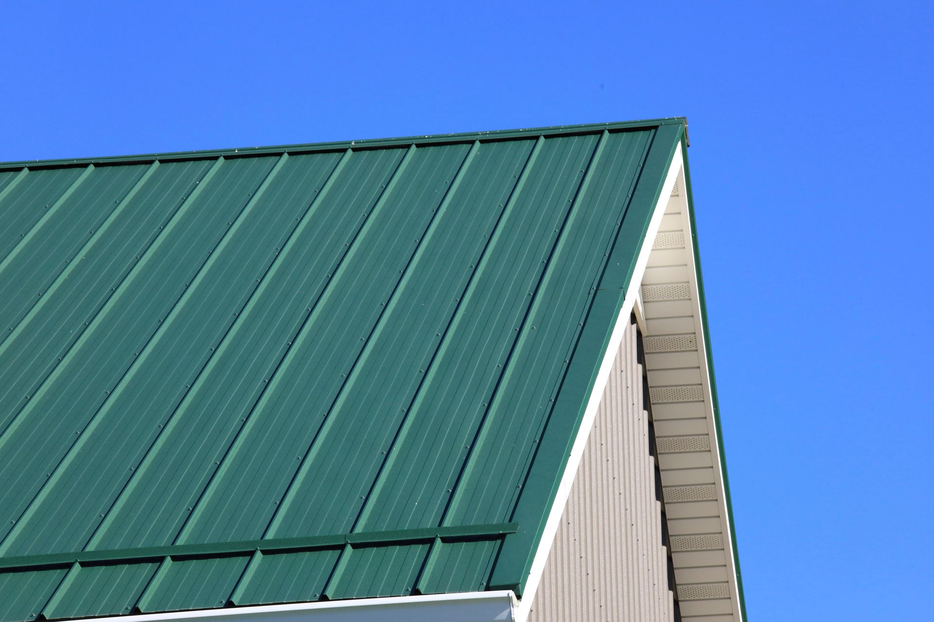Green metal roof on a building against a bright blue sky.
