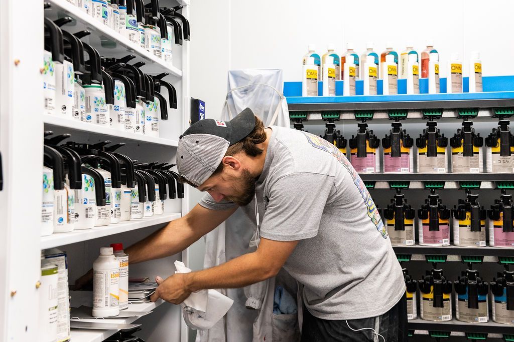 A man is standing in front of a shelf filled with bottles of paint.