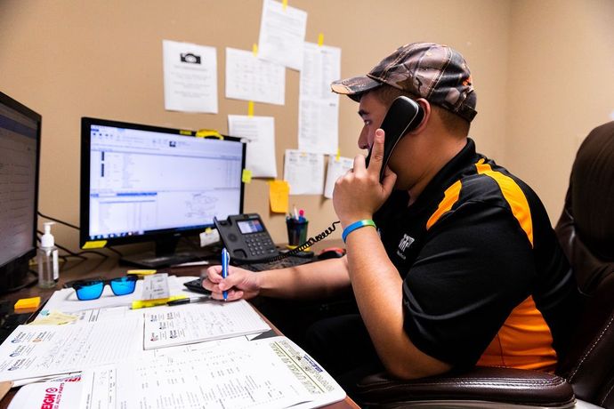 A man is sitting at a desk talking on a cell phone