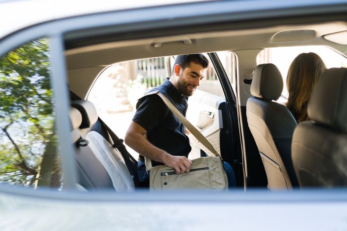 A man is putting his bag in the back seat of a car.