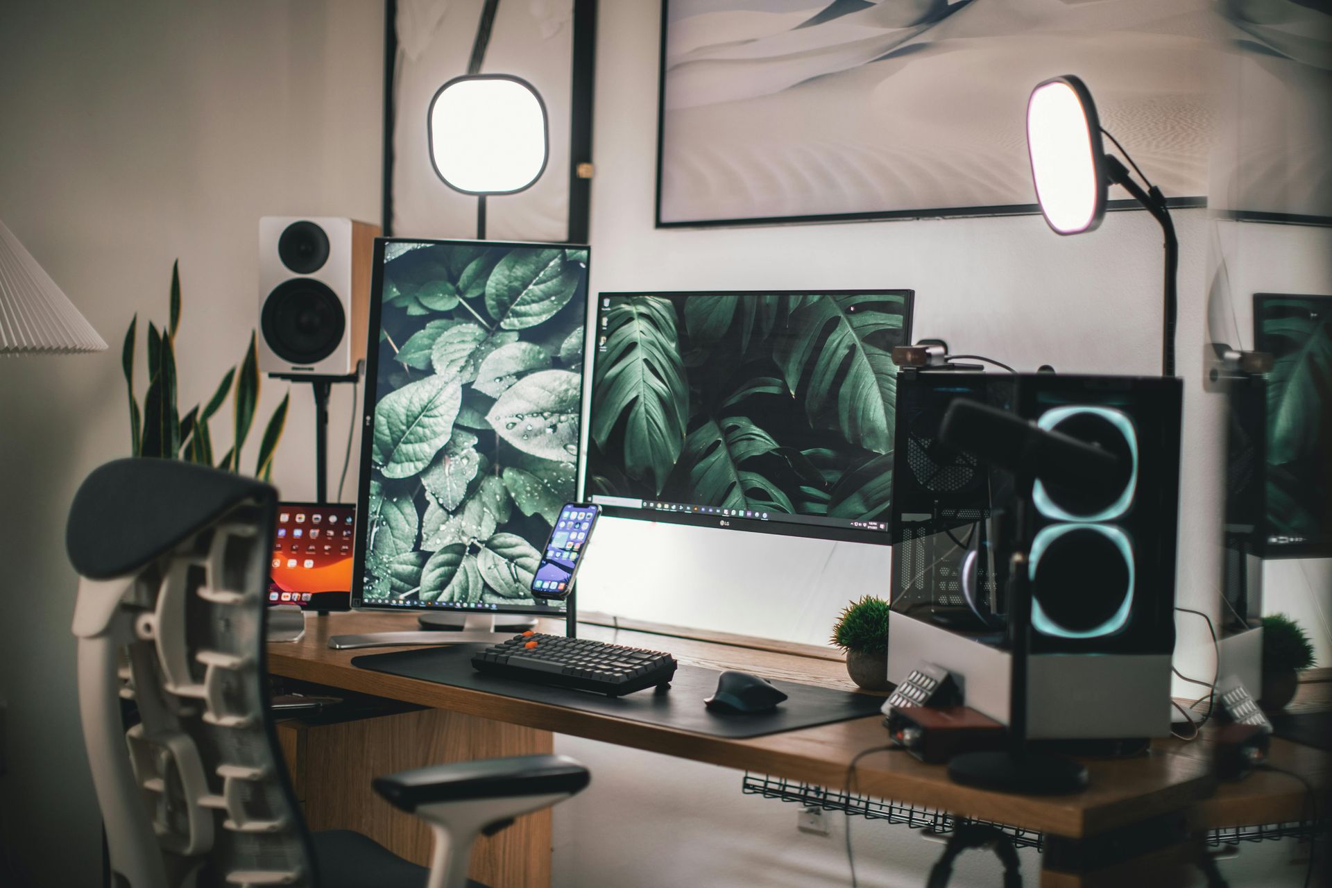 Modern home office setup with desk, monitors, PC tower, speakers, and plants.