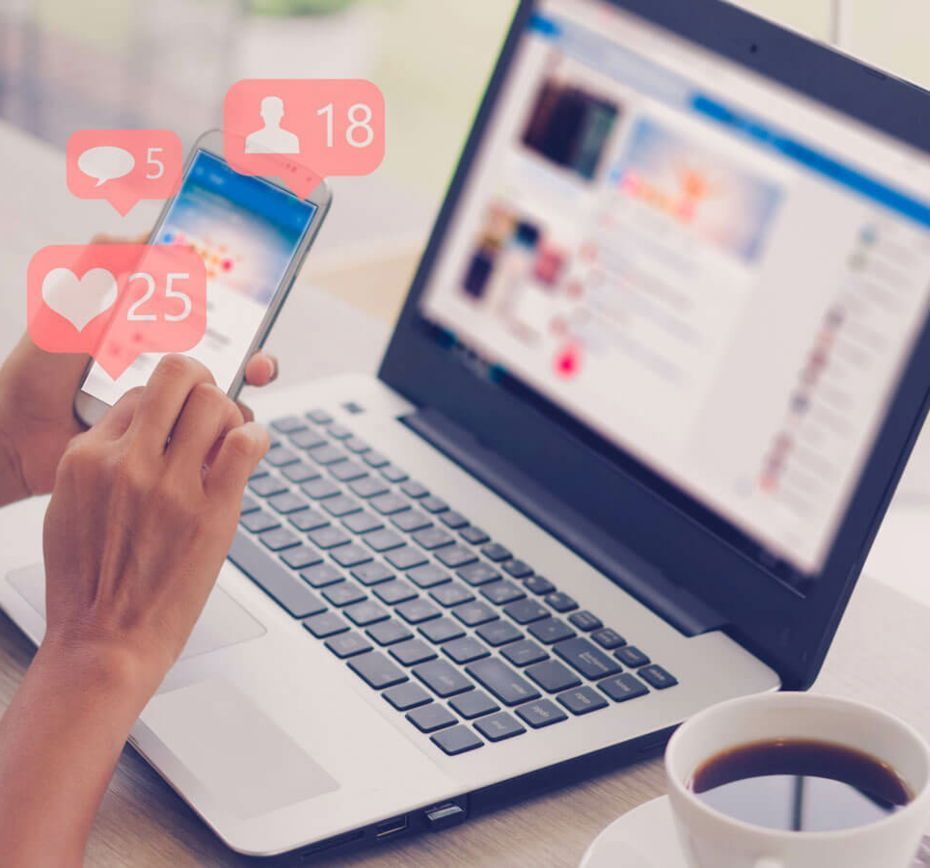 A person holding a cell phone in front of a laptop managing Social Media Marketing.