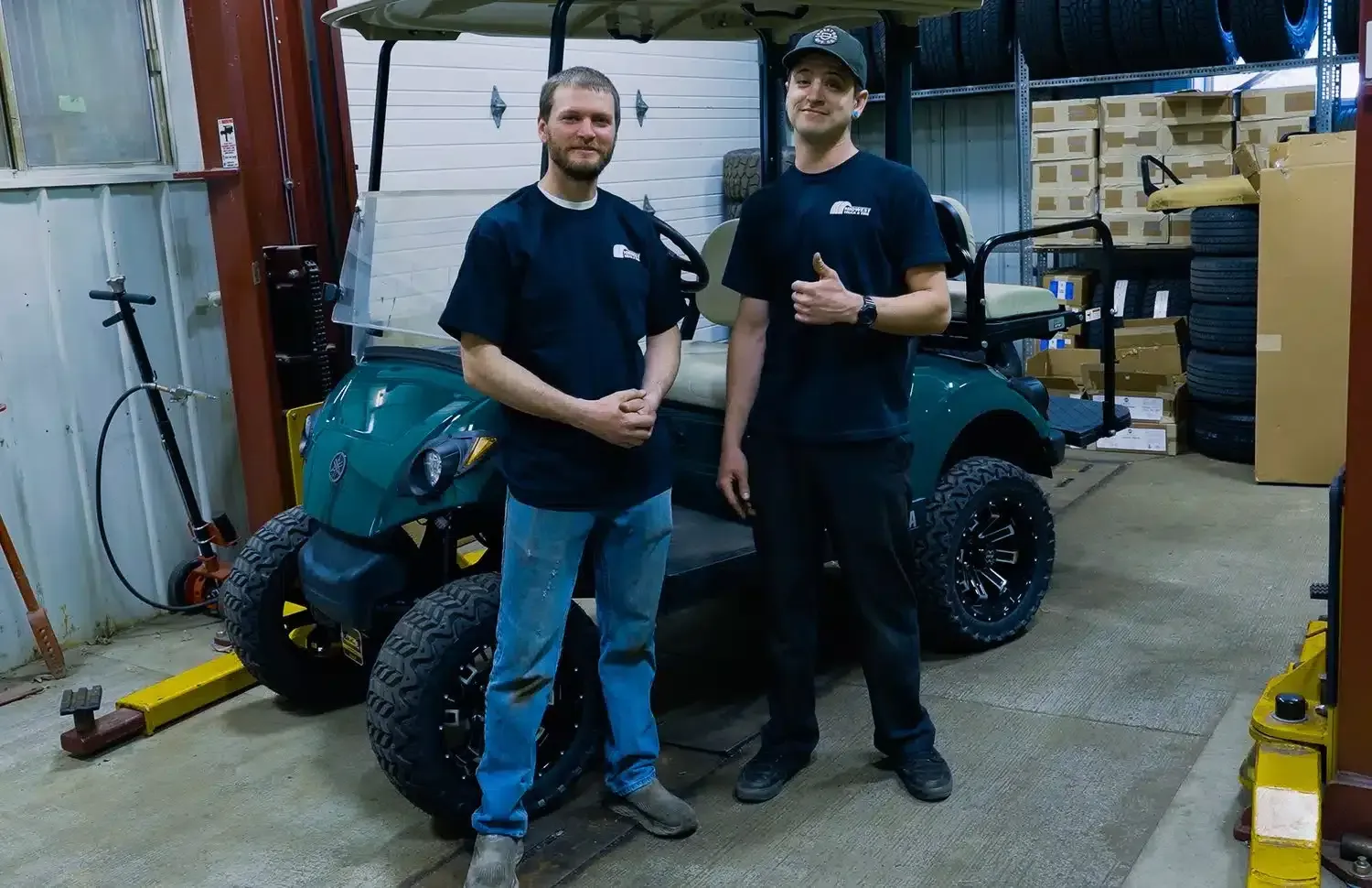Two men are standing next to a golf cart in a garage | Midwest Truck and Tire