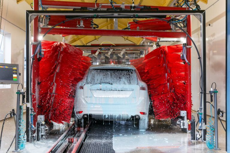 White car in an automatic car wash, surrounded by red brushes and soap, interior shot.