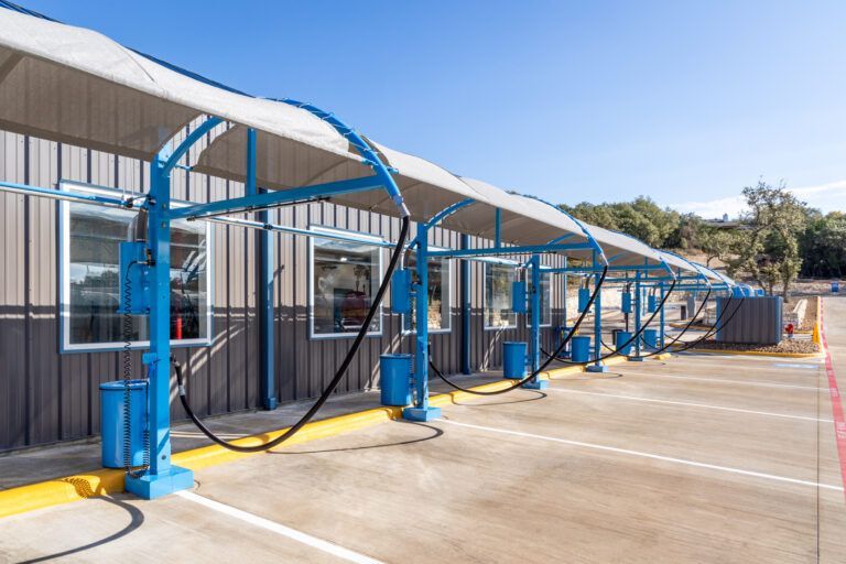 Blue car wash bays with overhead sun shades and service equipment on a paved lot.