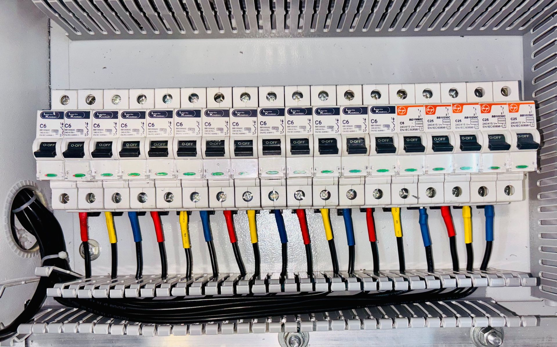 Electrical breaker panel with rows of labeled white circuit breakers and colored wires.