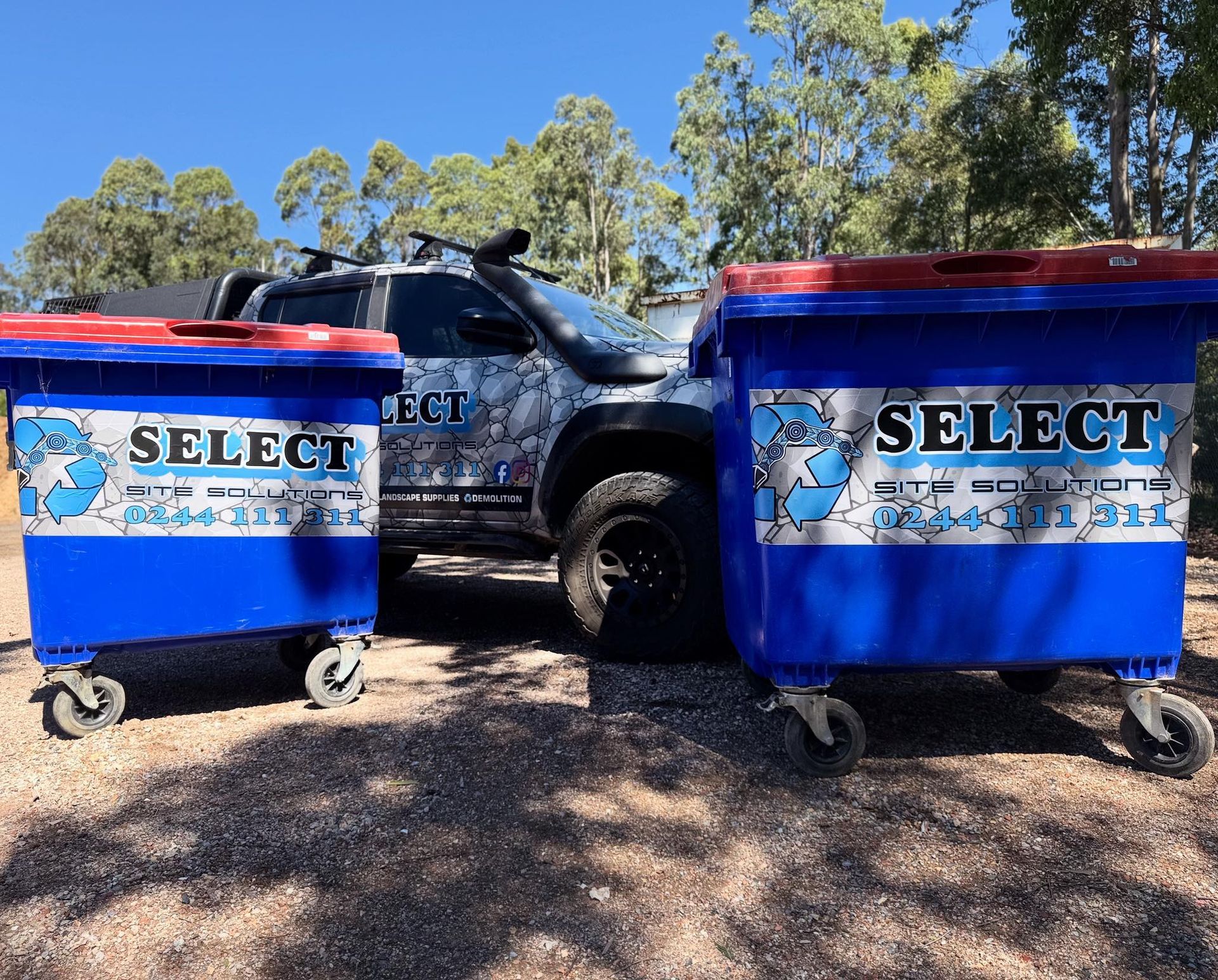 Two blue recycling bins with red lids and company logo next to a camouflaged truck outdoors. — Select Site Solutions in Kangaroo Valley, NSW