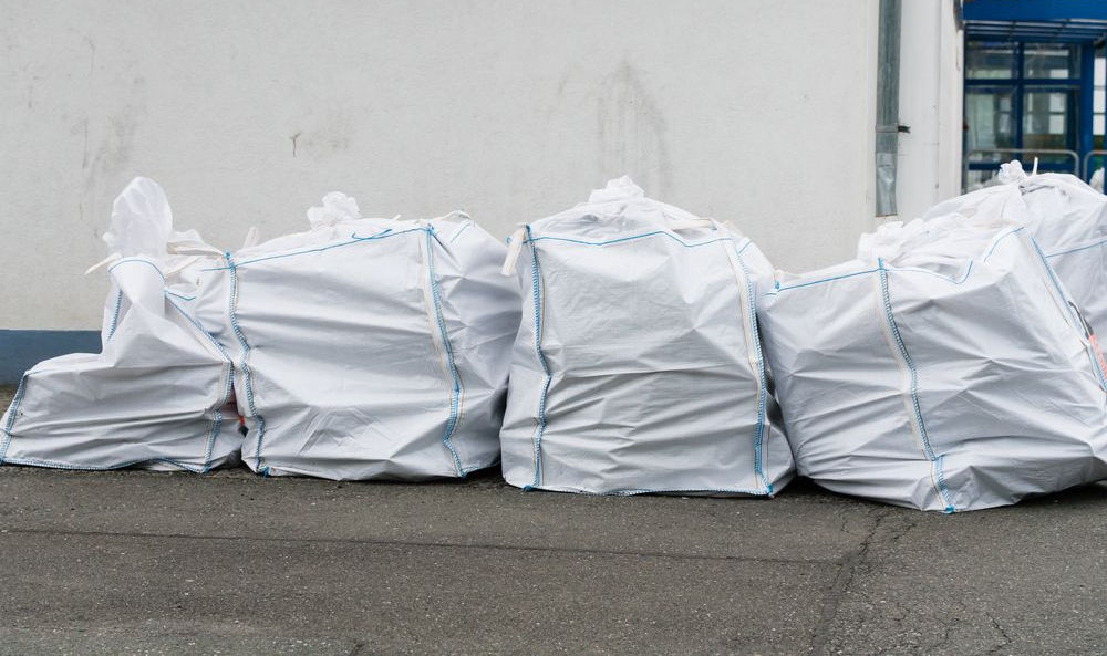 White bags filled and tied with blue twine, lined up against a white wall on a grey surface. — Select Site Solutions in Vincentia, NSW