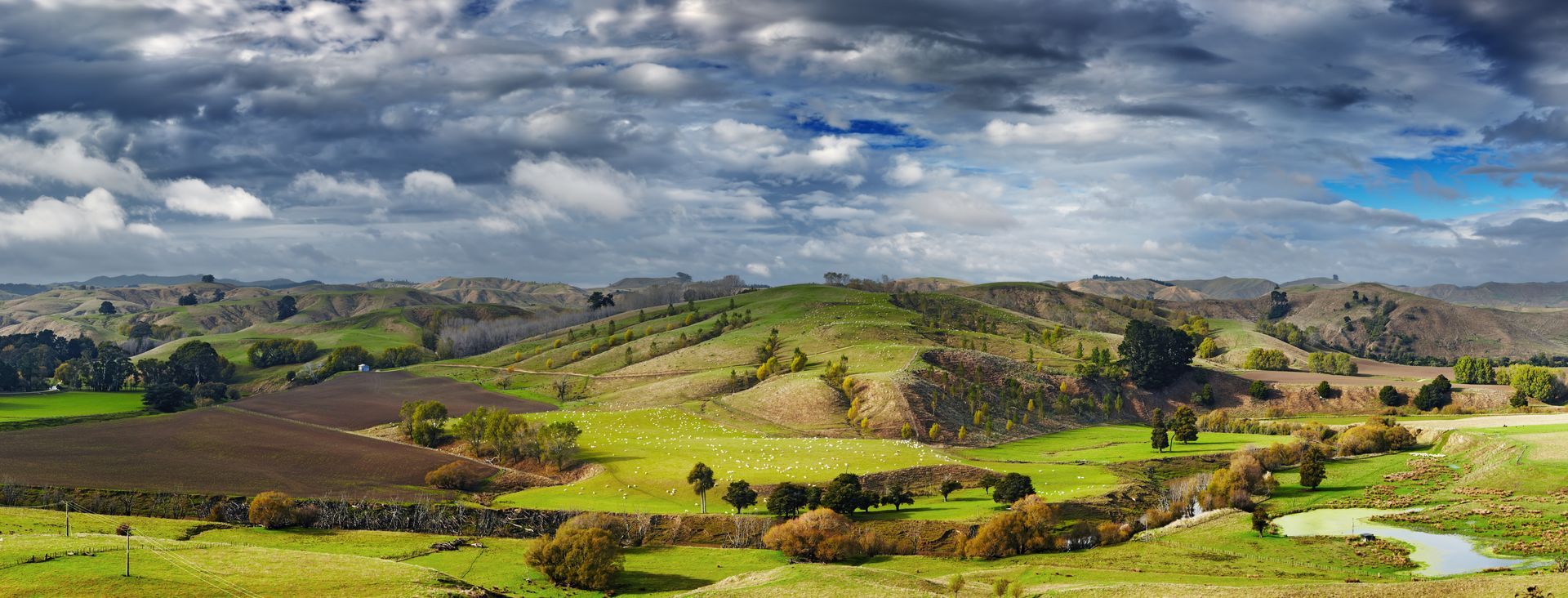 Green hills under a cloudy sky, with a stream running through the landscape.