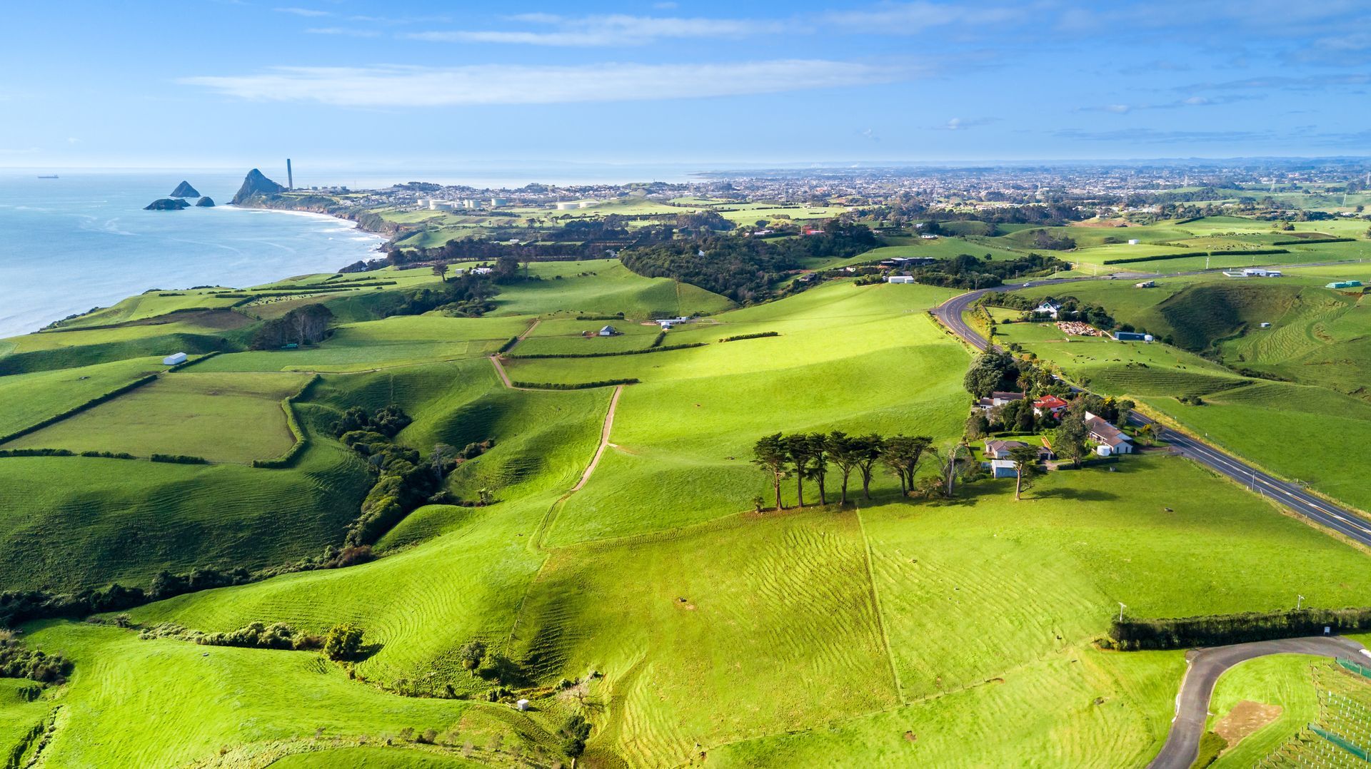 Green fields rolling towards a coastline under a bright blue sky, with a road and town visible.