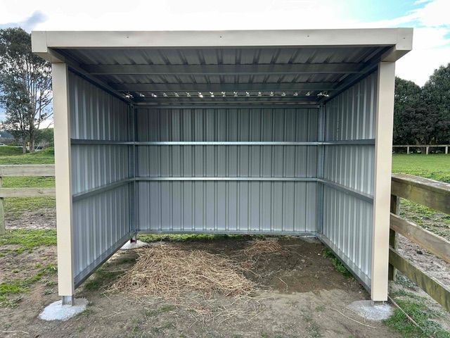 Metal shed with corrugated walls, hay on the ground, in a grassy field.