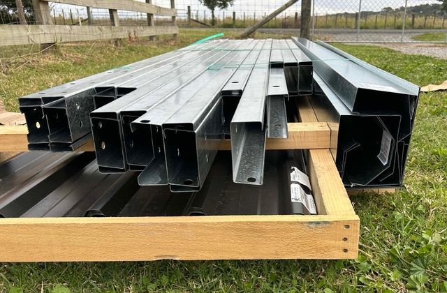 Metal framing and dark sheets stacked on a wooden base outdoors.