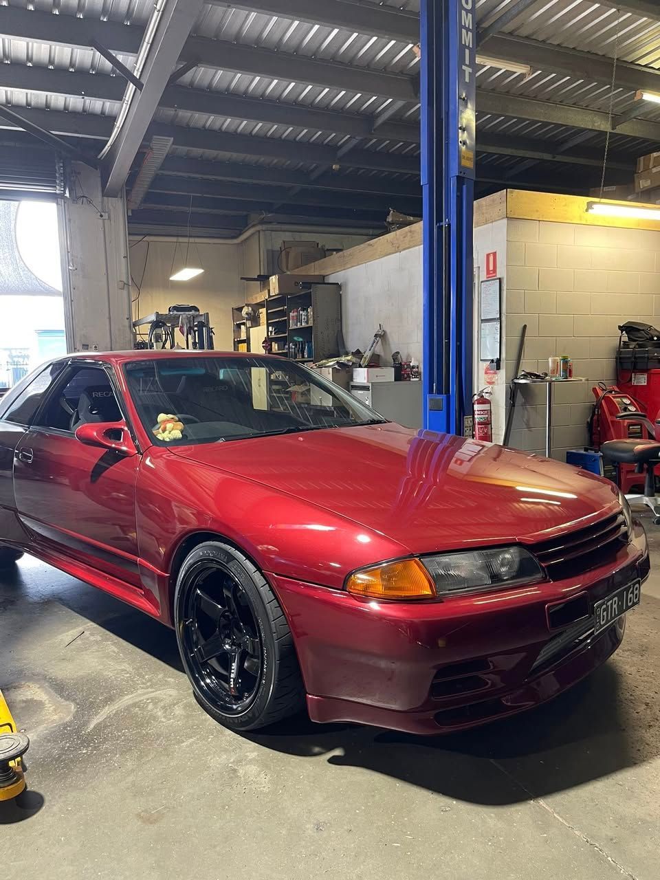 Red Nissan Skyline R32 car in a garage with black wheels.