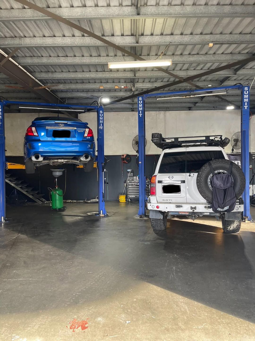 Blue car on a lift and white SUV in an auto shop.