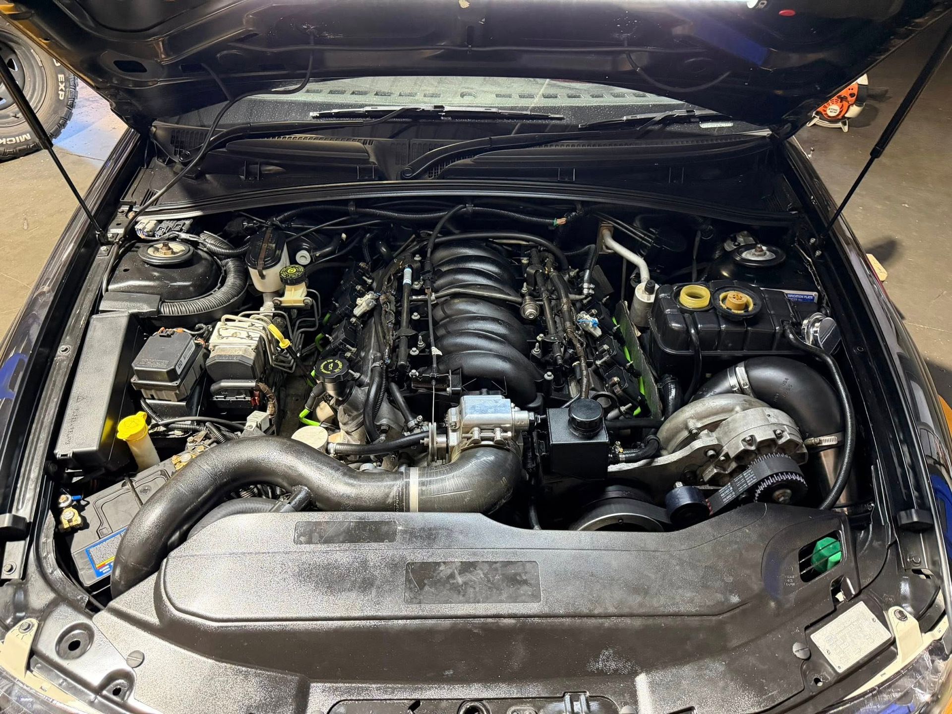 Black car engine with open hood, showing complex mechanical components.