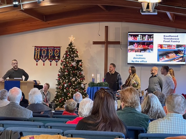 Church service with a group of people, Christmas tree, cross, and food pantry sign.