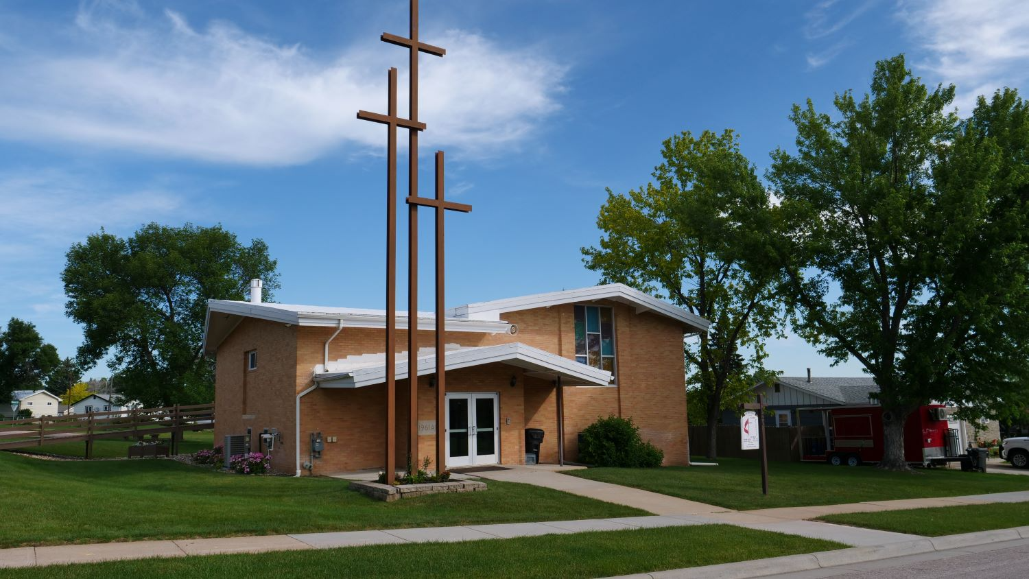 Brick church with three crosses in front, under a blue sky.