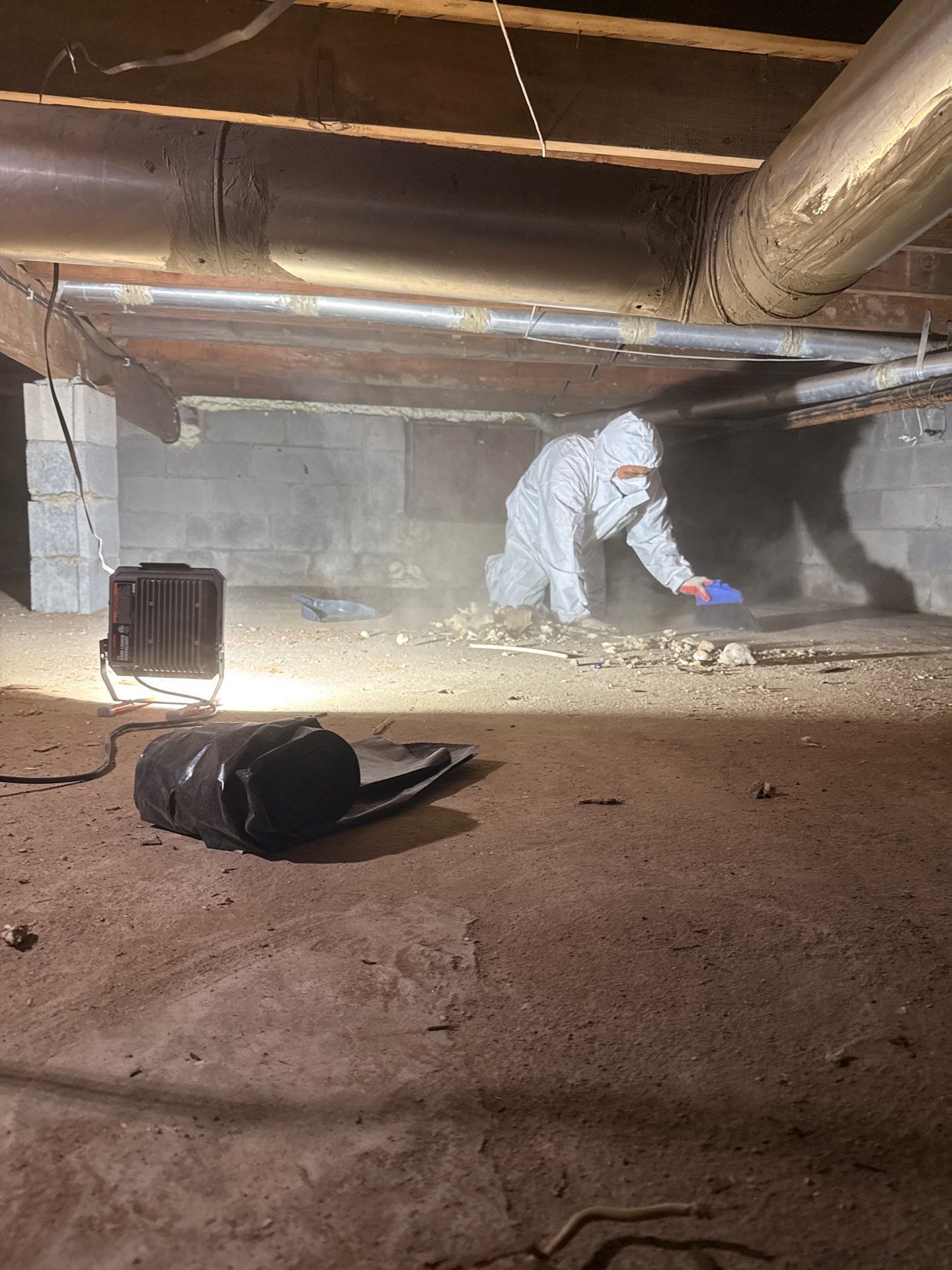 Person in protective suit working under a house, dusty environment.