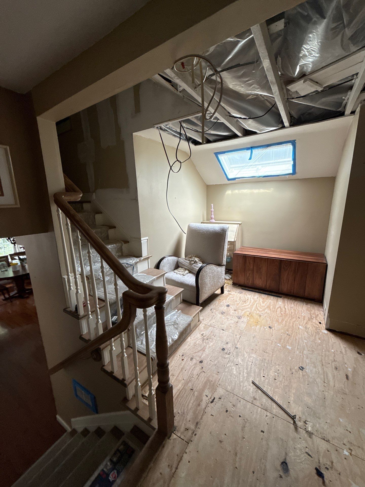 Staircase with a sitting area at the top, chair, chest, skylight, and exposed ceiling, under construction.