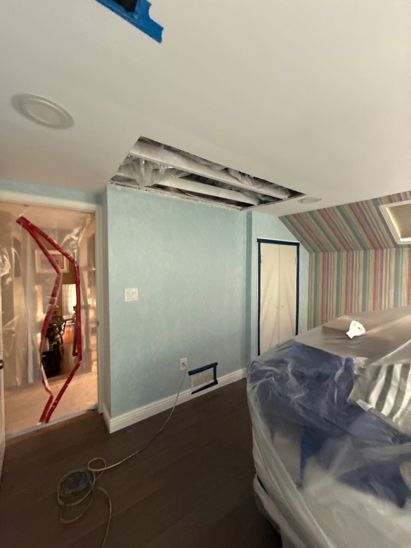 Room under renovation with exposed ceiling beams, blue walls, and dark wood floor.