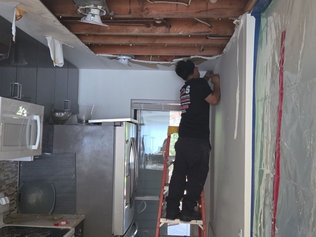 K.O.S. Restoration technician removing water-damaged ceiling in Westhampton Beach condominium kitchen