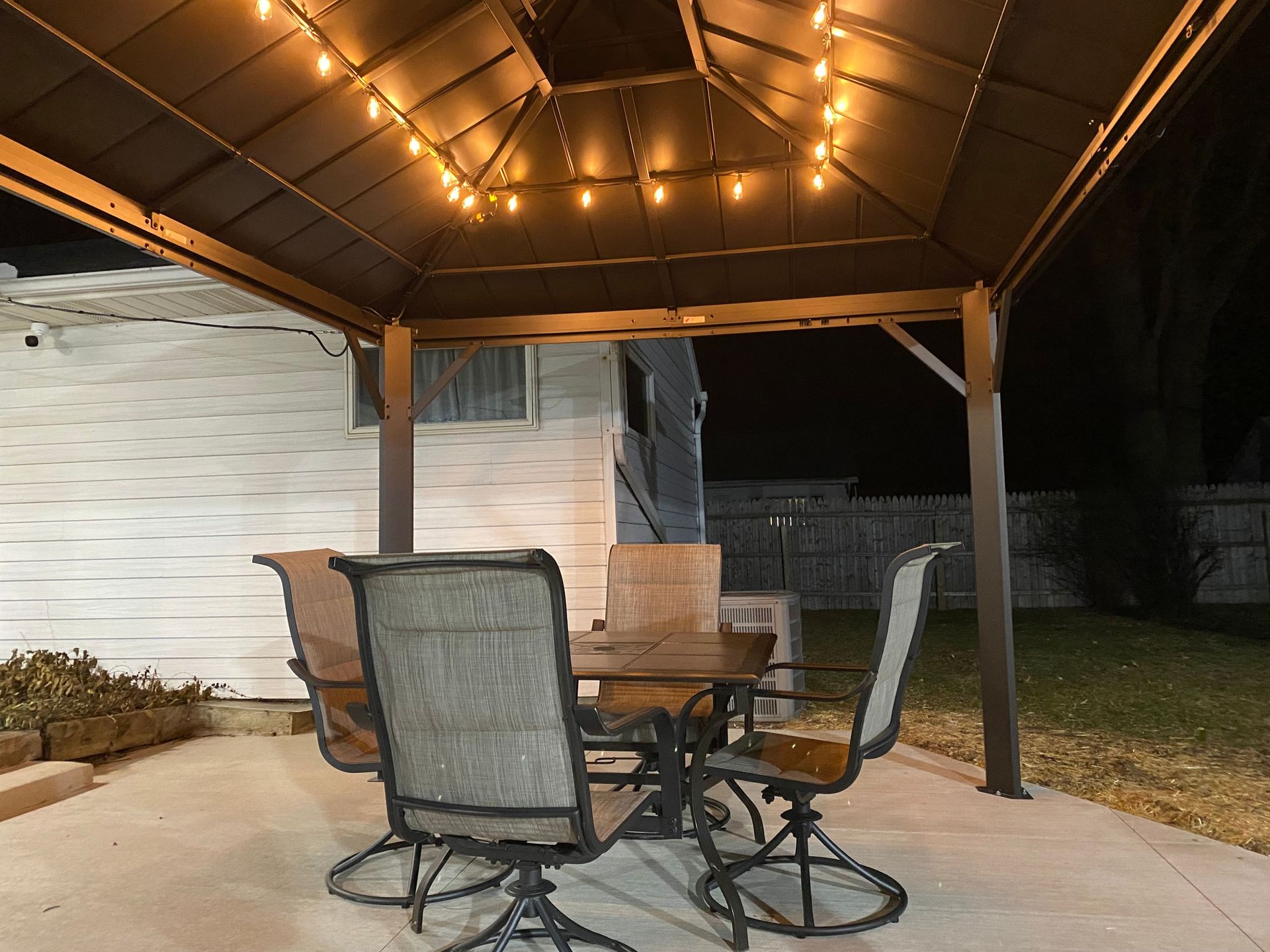 A gazebo with a table and chairs underneath it at night.
