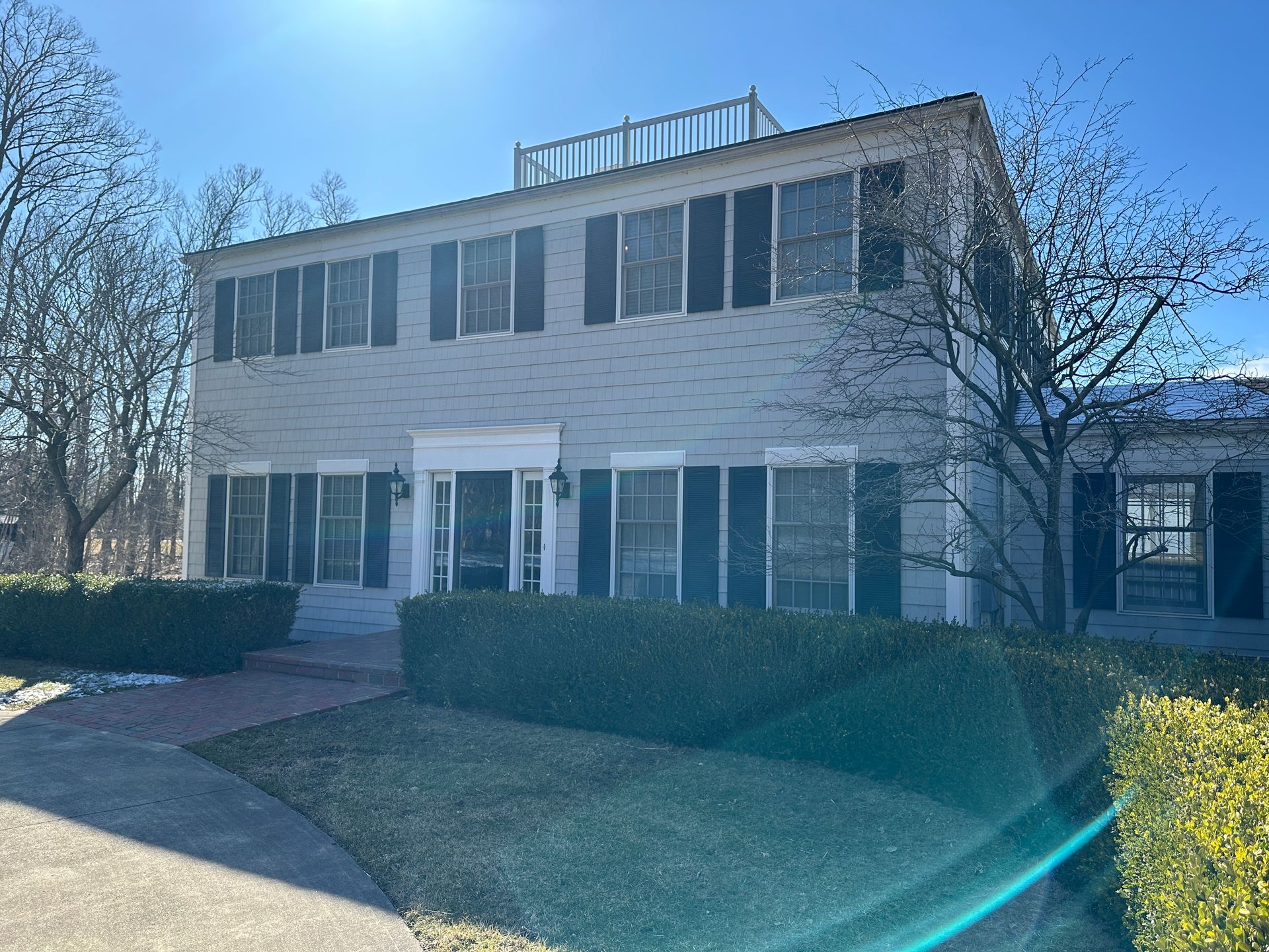 A large white house with black shutters and a blue sky in the background